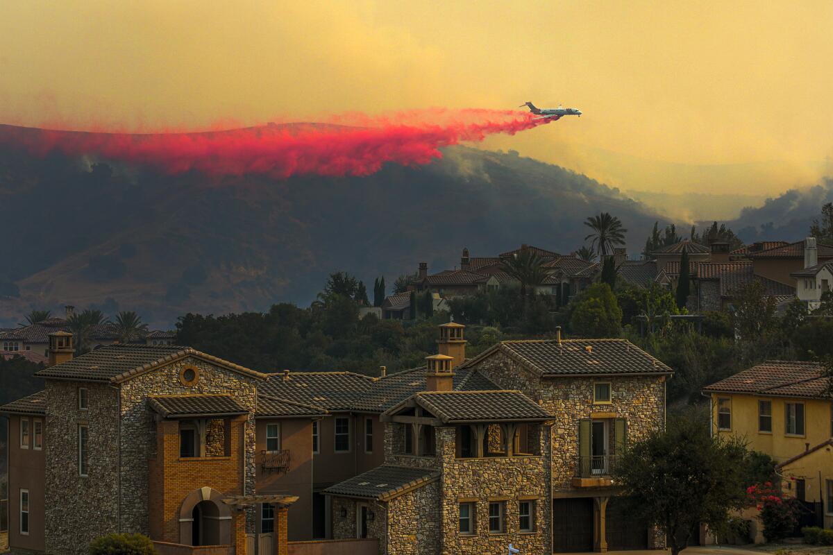 An air tanker drops a trail of red fire retardant against a hazy sky behind homes in Chino Hills