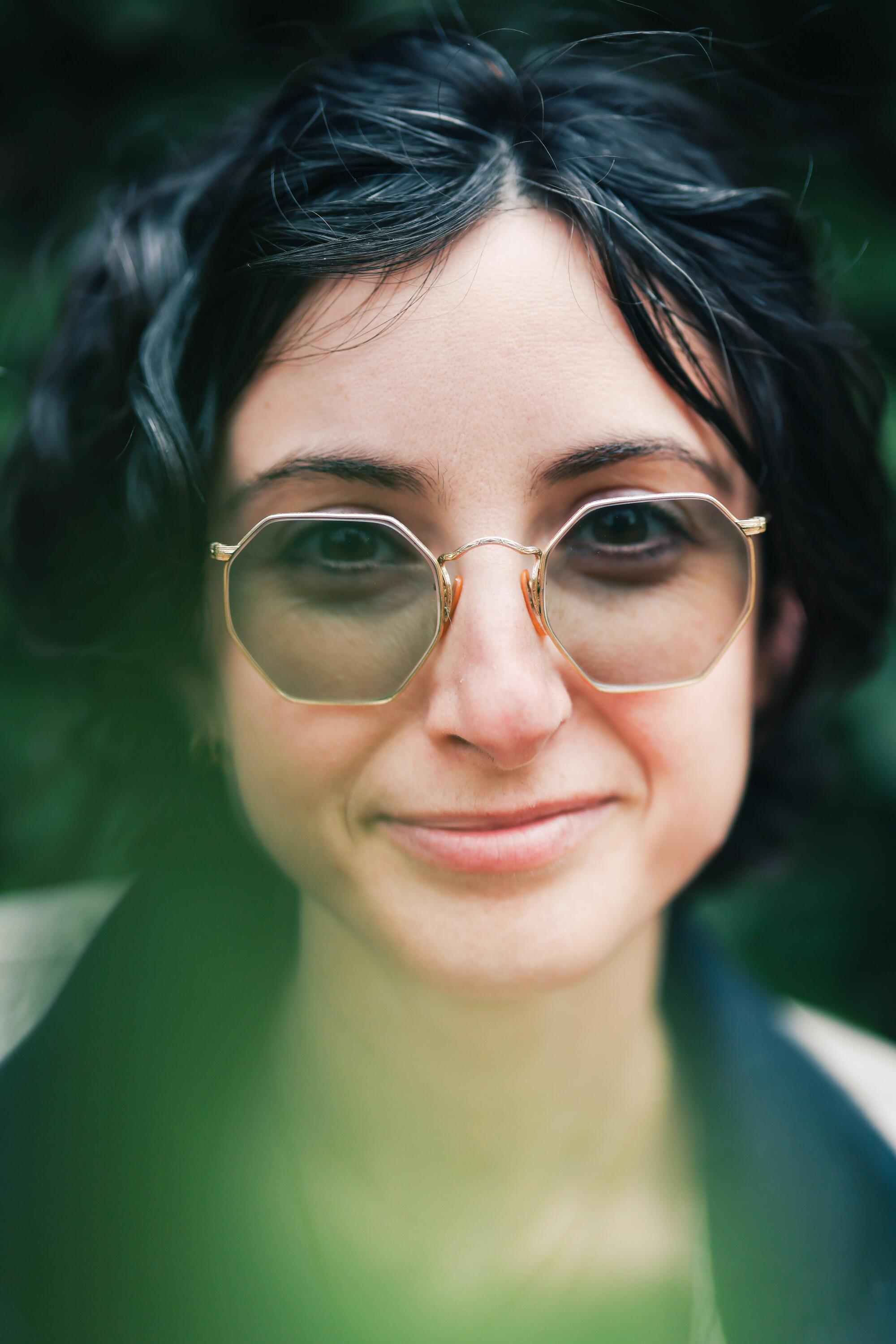 A slightly smiling woman wearing hexagonal sunglasses