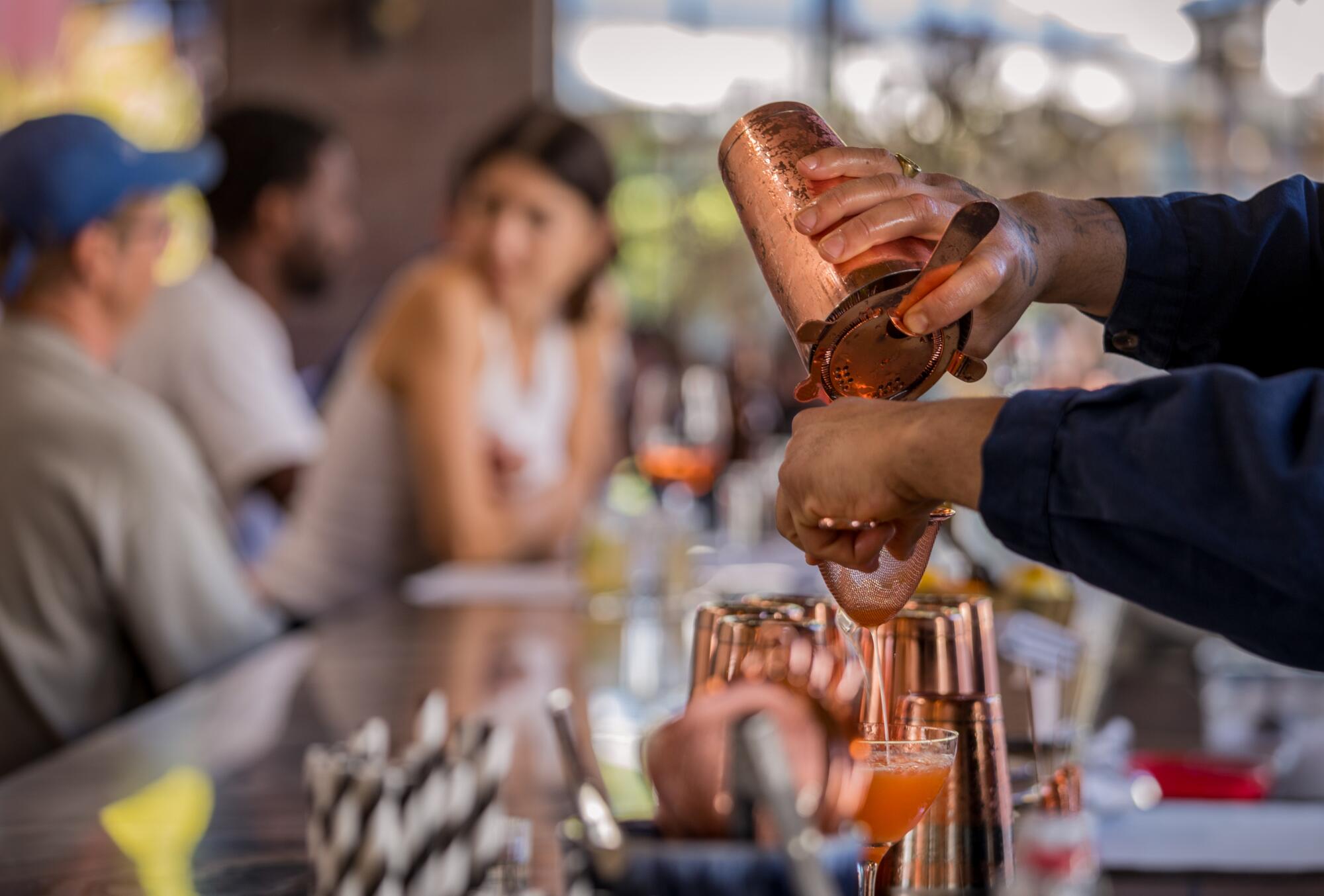 A bartender pours a cocktail from behind the counter of Loreto's front-and-center bar. 