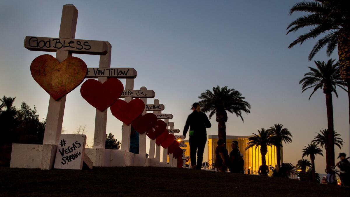 With Mandalay Bay Resort and Casino ahead of her, a woman runs her hand over the top of wooden crosses bearing the names of those killed in the 2017 mass shooting.