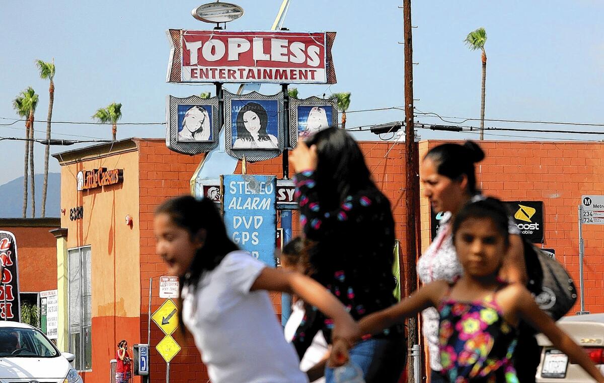 A sign for an adult entertainment business looms behind women and children crossing at Roscoe Boulevard and Sepulveda Boulevard in the San Fernando Valley.