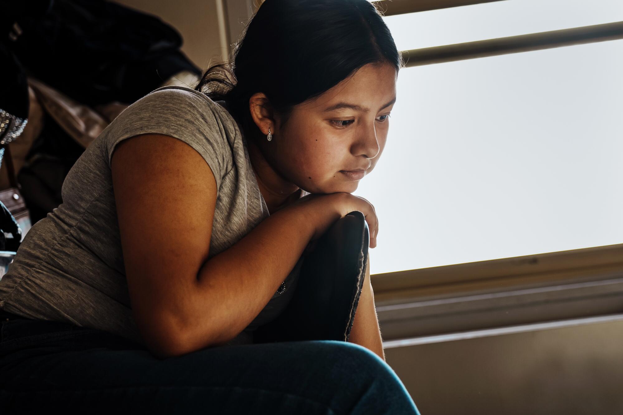 A girl sits on a chair and looks at the floor.