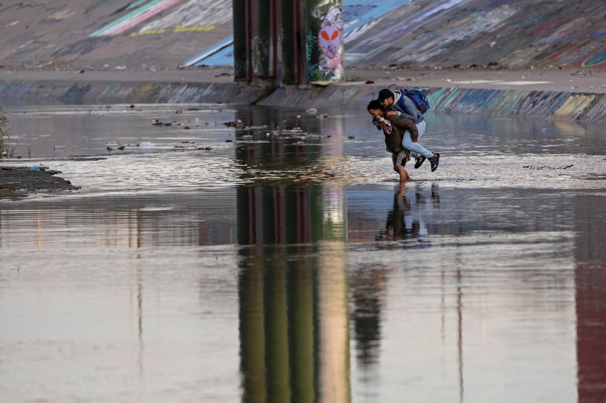 A person carries another person on their back while crossing a river 