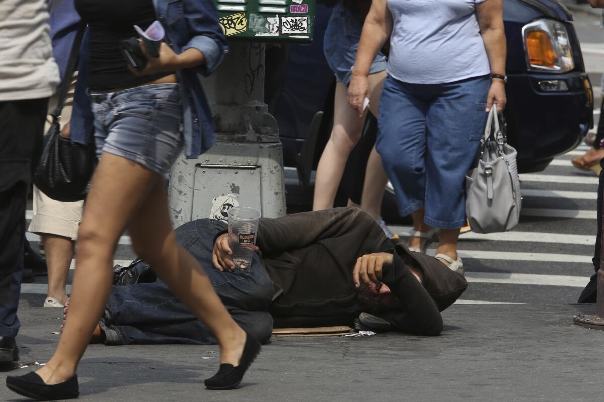 La gente camina junto a un indigente tirado en el suelo que pide dinero en la calle 14 de Nueva York el 4 de septiembre del 2015. Las redes sociales se han convertido en un intrumento para difundir fotos e información de los indigentes, que para muchos son una violación de sus derechos.