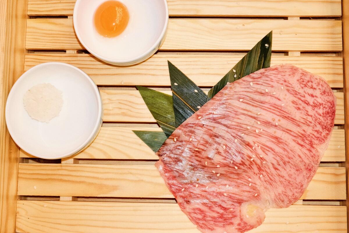 An overhead photo of a thin, large slice of raw Wagyu in a wood box at Hibiki BBQ in San Gabriel with egg yolk and small rice