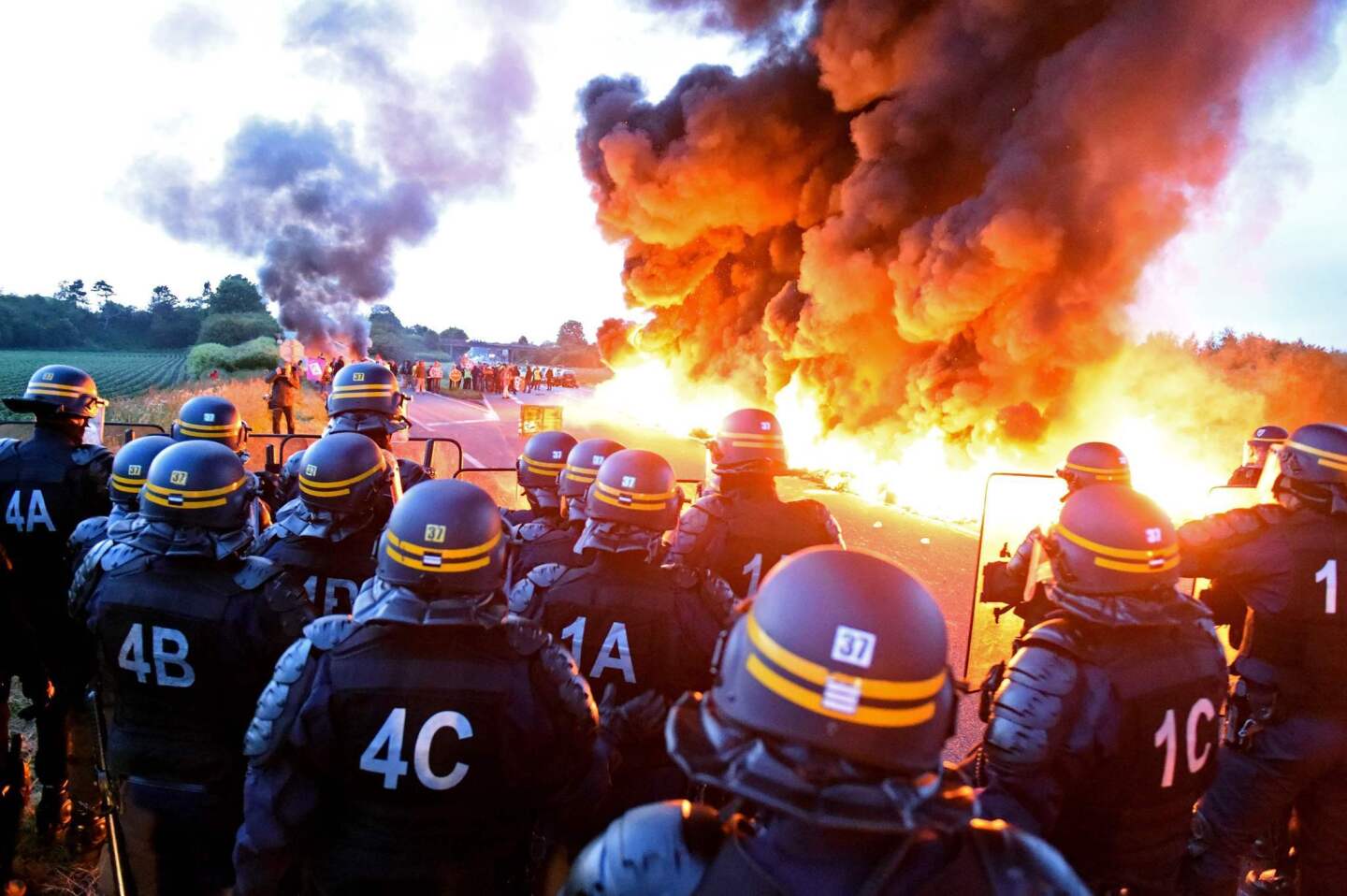 Riot police watch as a fire set by striking refinery workers burns during a blockade of the oil depot of Douchy-Les-Mines. Workers are protesting the government's proposed labor reforms.