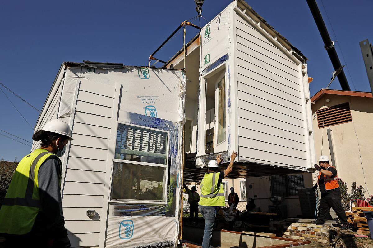 Workers lower part of a prefabricated ADU onto a lot.