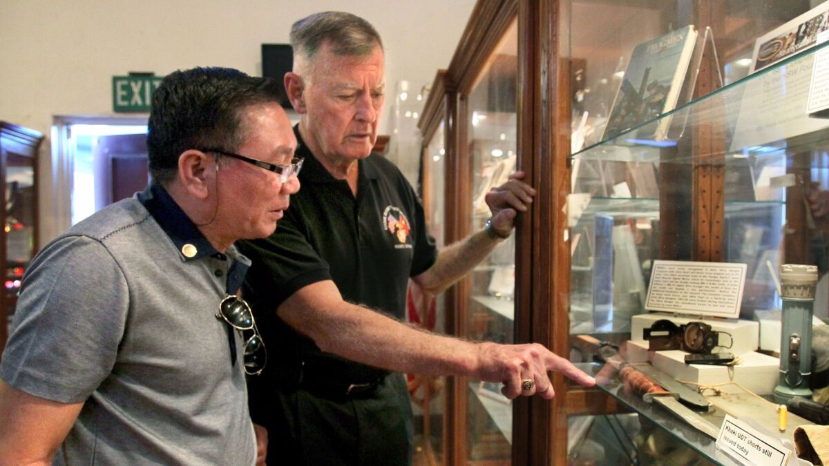 In this 2014 photo, retired Brig. Gen. Mike Neil, right, shows his visitor, "GTO," whom Neil's Marine unit "adopted" in Vietnam as a boy, the display of Vietnam war items at the San Diego Veterans Museum & Memorial Center.