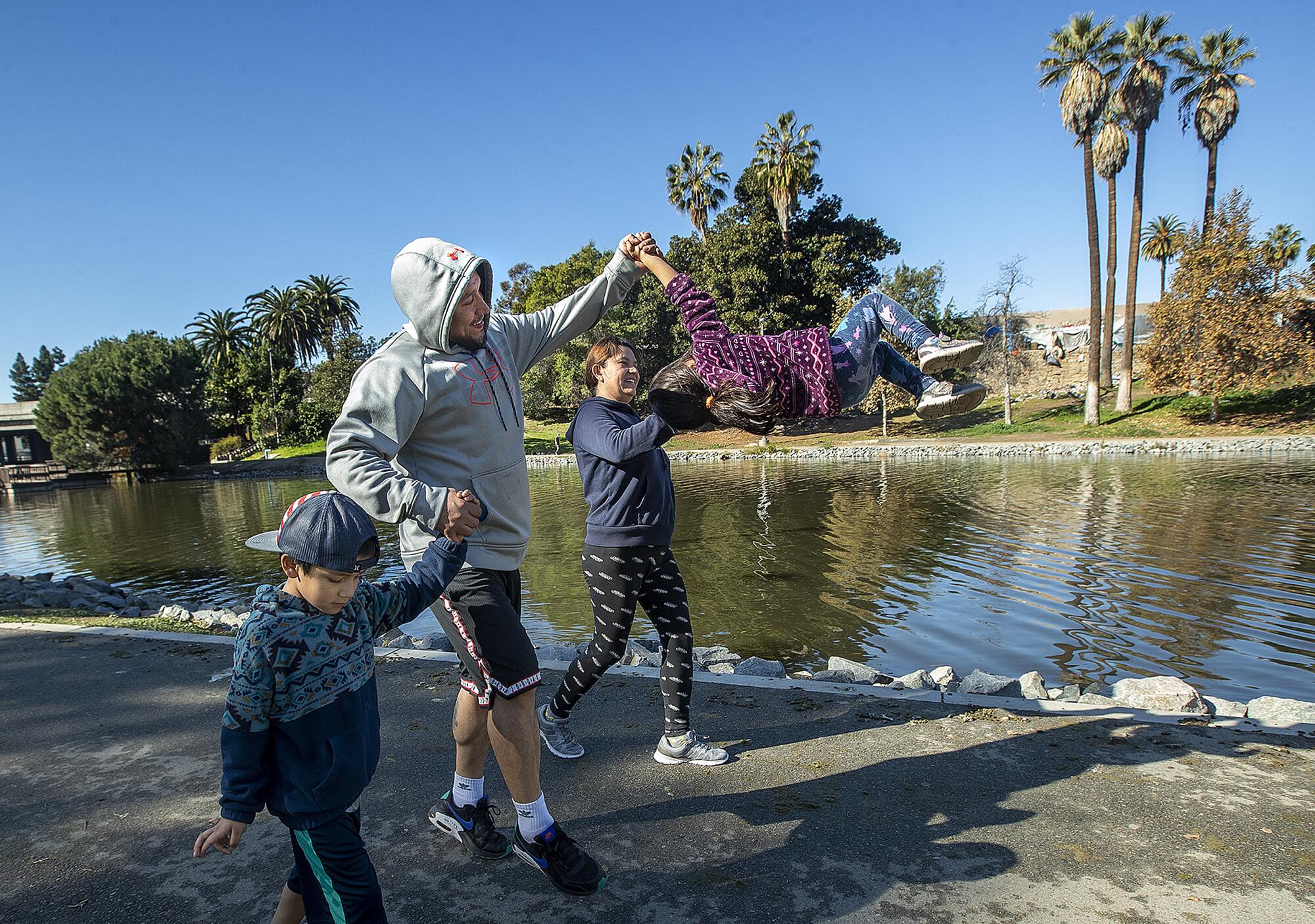 A girl is lifted up by her parents while walking along a lake