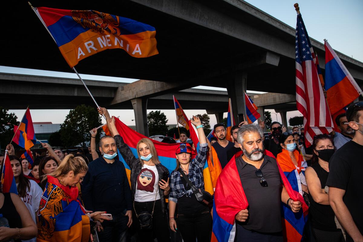 Protesters wave red blue and orange Armenian flags and U.S. flags near a freeway overpass