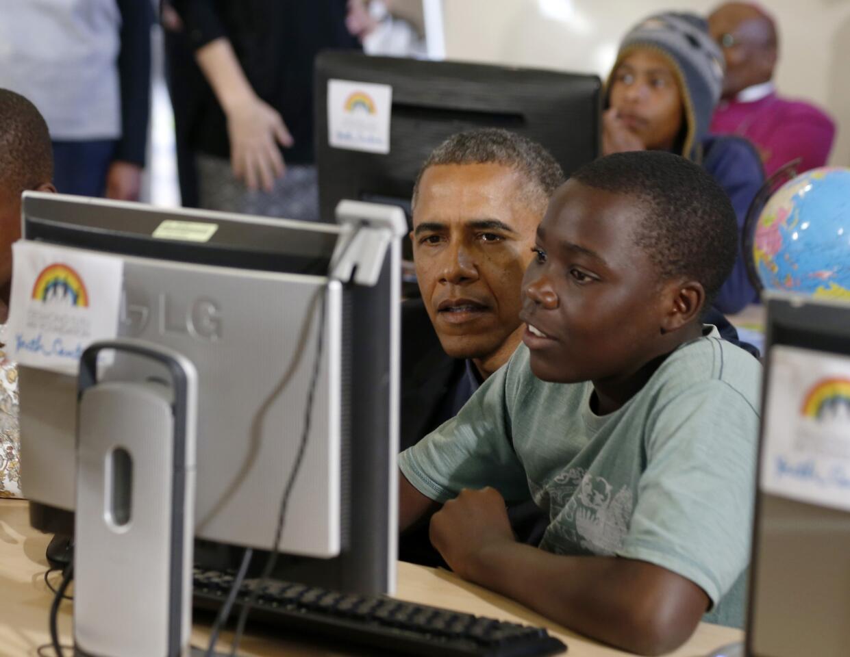 U.S. President Barack Obama looks at a computer with youth as he tours the Desmond Tutu HIV Foundation Youth Centre and takes part in a health event in Cape Town
