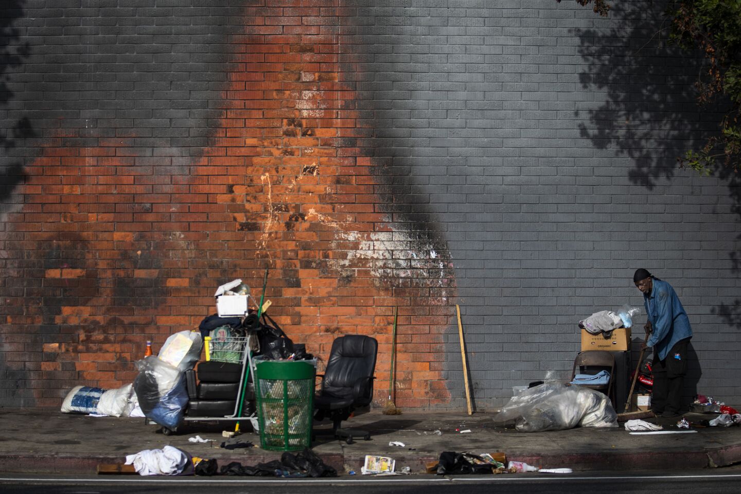 LOS ANGELES, CALIF. - NOVEMBER 12: Robert Taylor is cleaning around his encapment near the corner of 39th and Broadway in Los Angeles, Calif. on Tuesday, Nov. 12, 2019. The paint on the building next to where he sleeps on the sidewalk remains chard following a fire. Still he remains positive. He has been working with outreach workers on getting housing. (Francine Orr / Los Angeles Times)