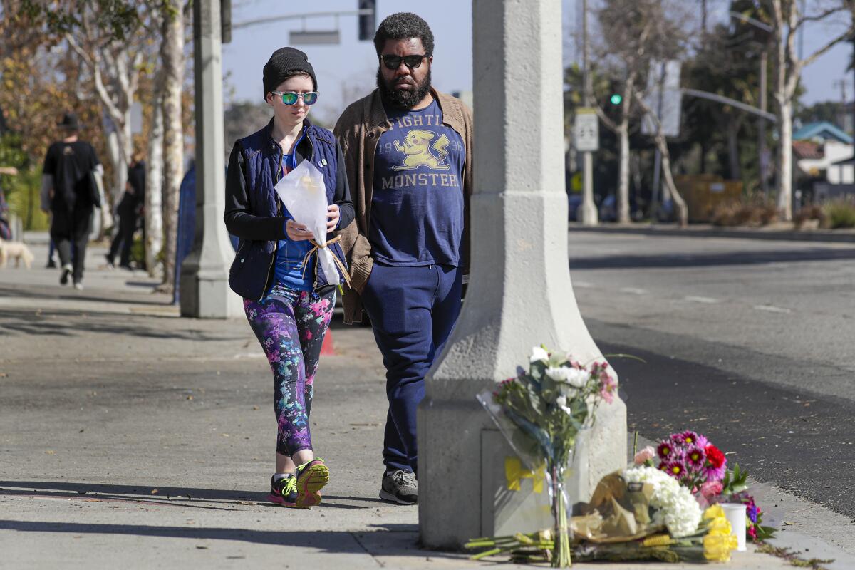 Two people bring flowers to a makeshift memorial on a sidewalk. 