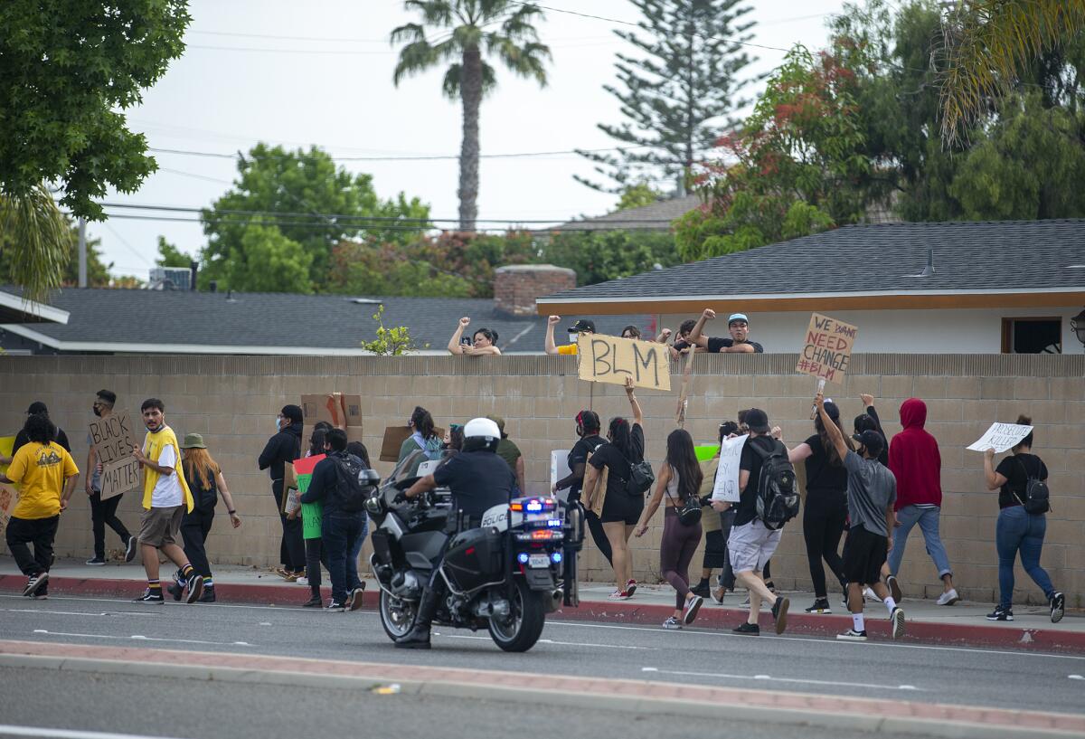 Protesters walk along Fairview Rd. as a Costa Mesa police officer patrols the street on Tuesday.