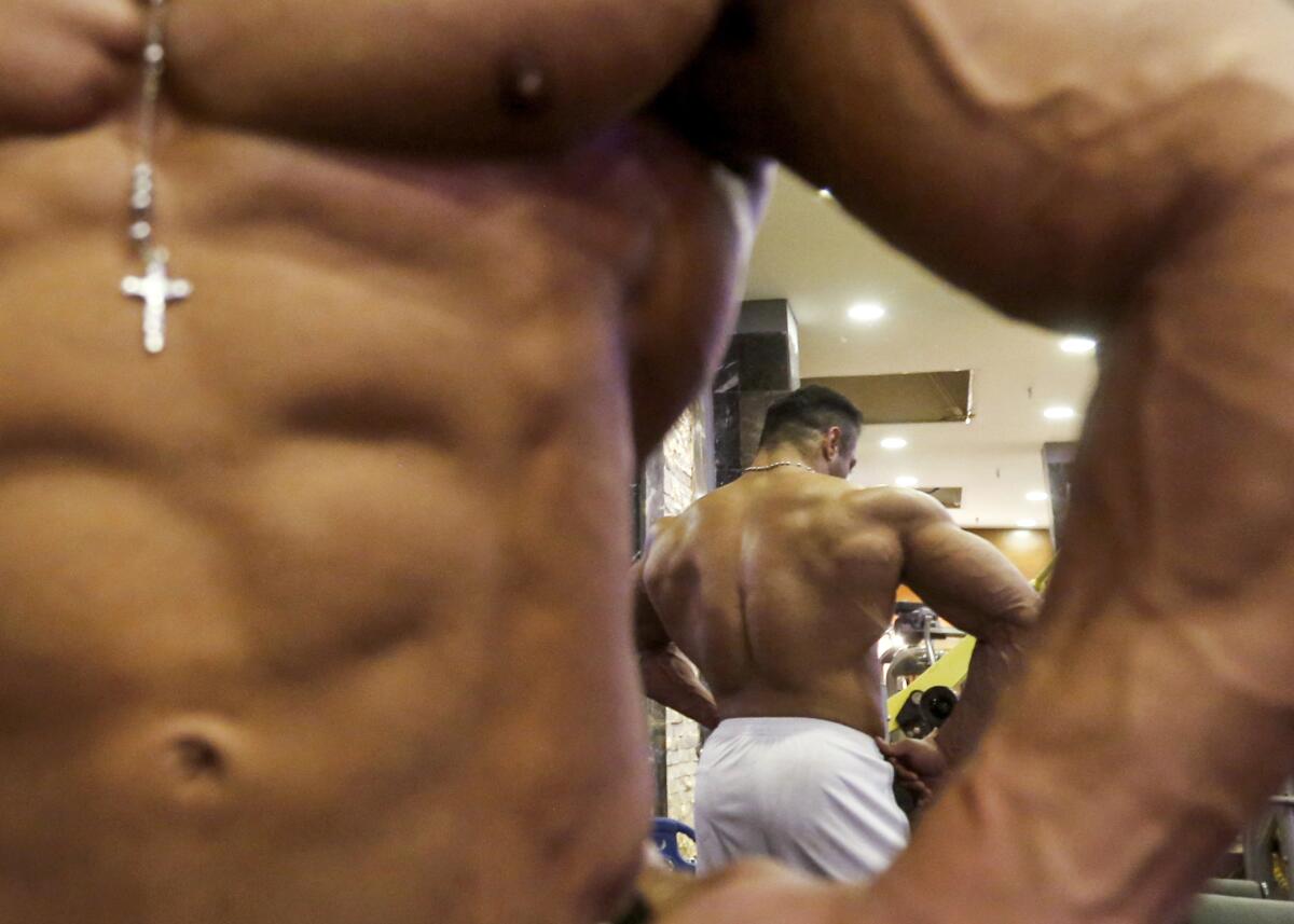 Close-up of a bodybuilder, also seen reflected from behind.