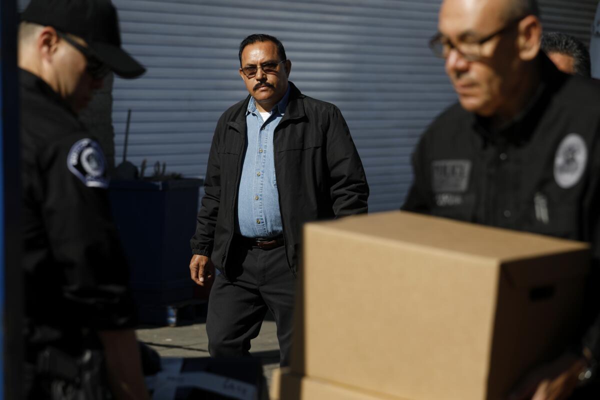 Agents carry boxes out of an auto shop as the owner looks on