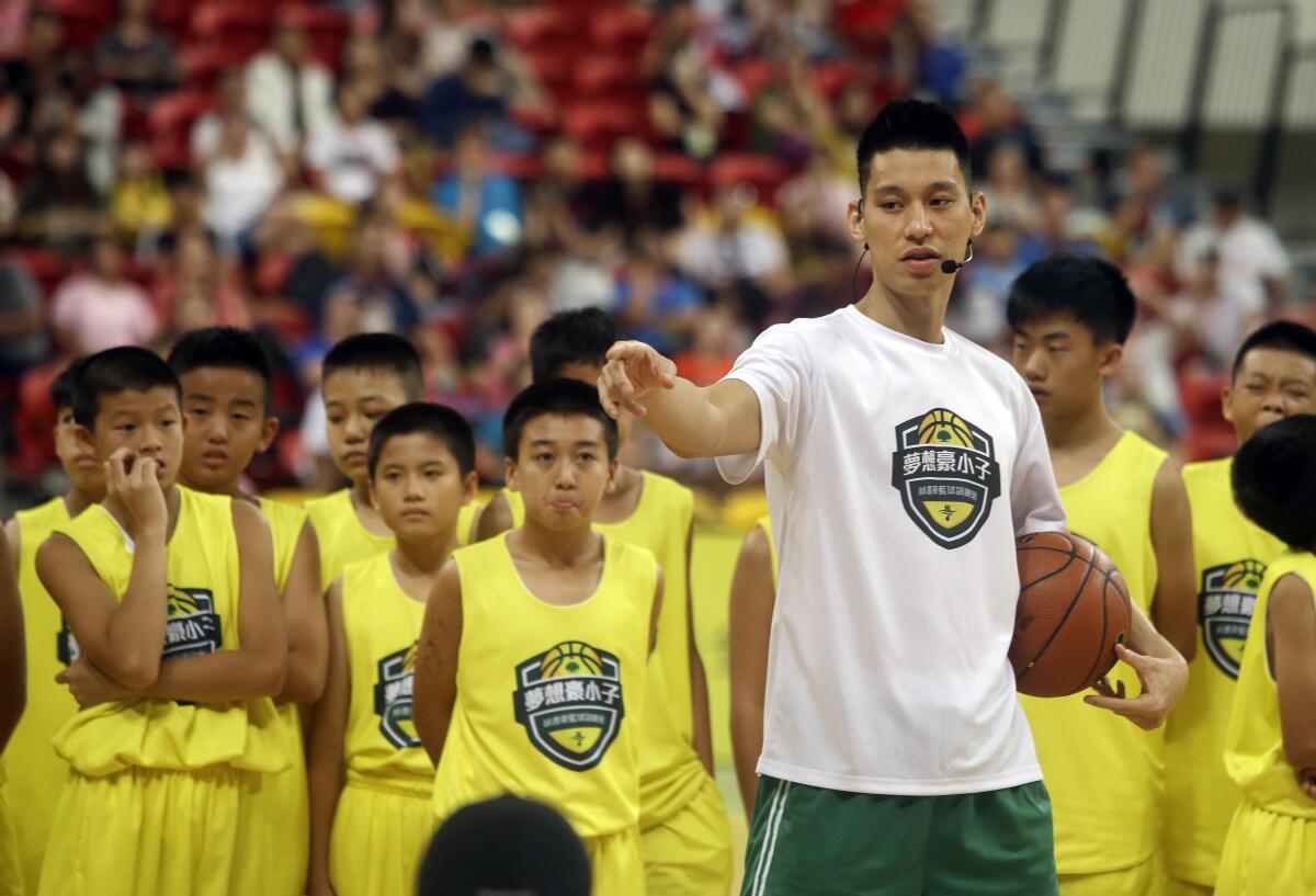 A man in a T-shirt holds a basketball and points. About a dozen young boys in matching basketball uniforms look on.