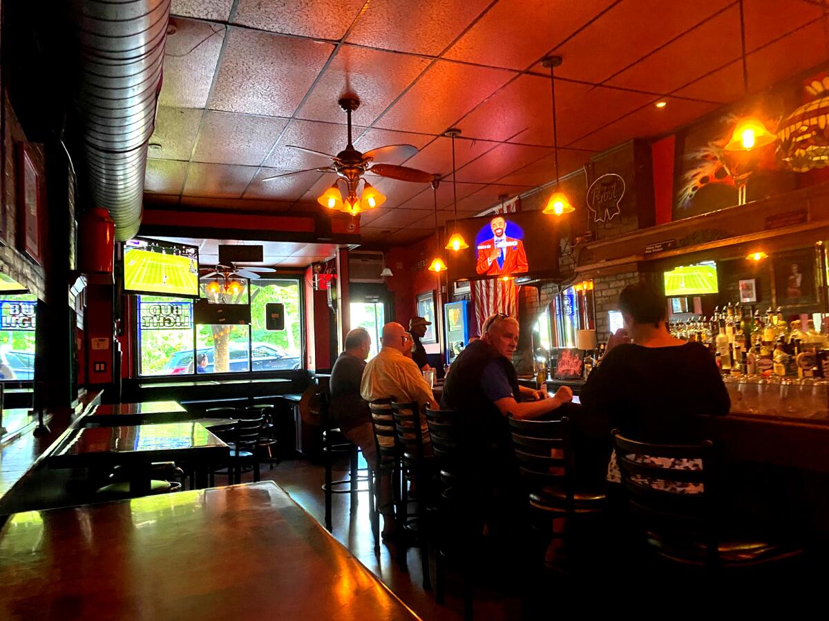 Several people sit on barstools inside a dimly lit bar.