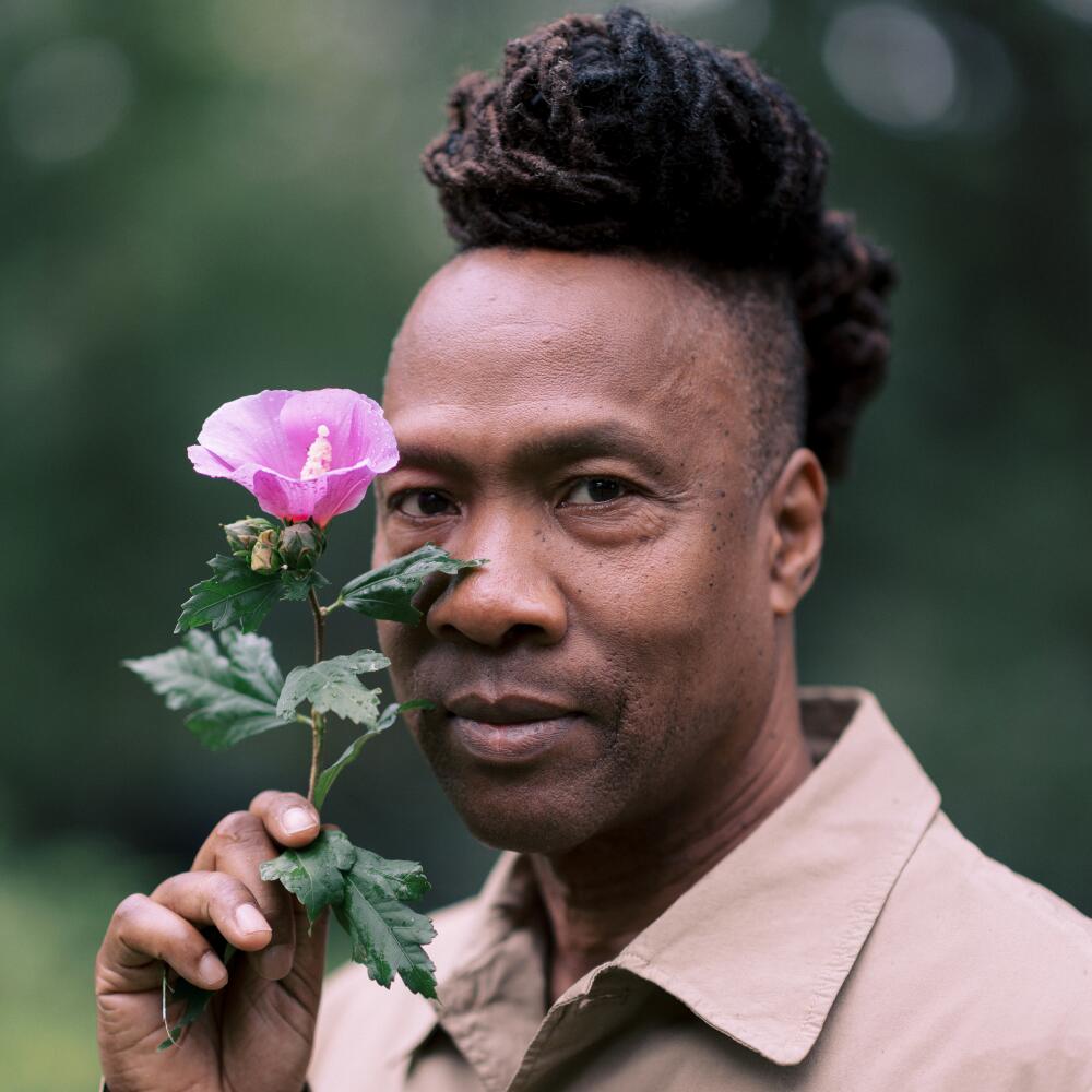 A man stands outside holding a purple flower to his face.