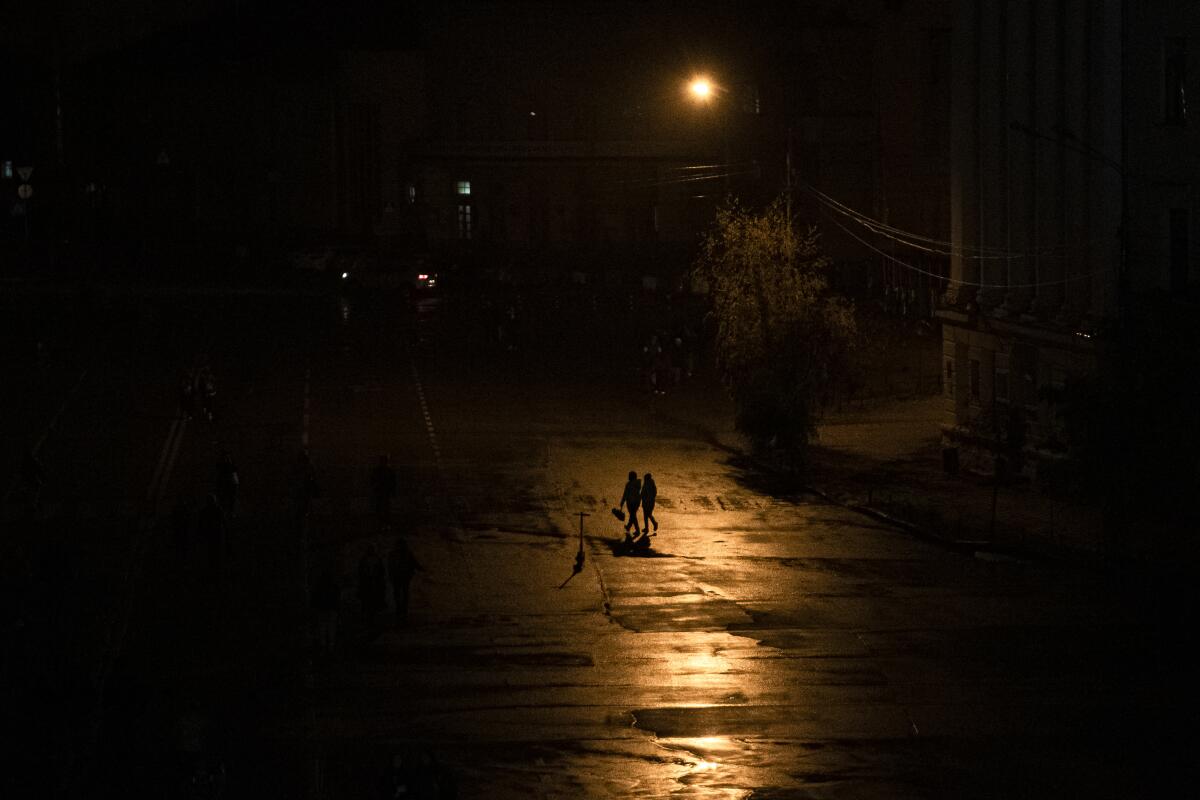 Silhouette of two people walking across a street during a blackout in Kyiv