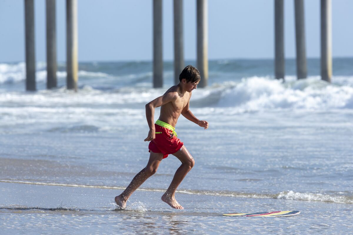 Gus Wood from Salt Lake City, Utah skim boards at Huntington Beach near the pier on Monday.