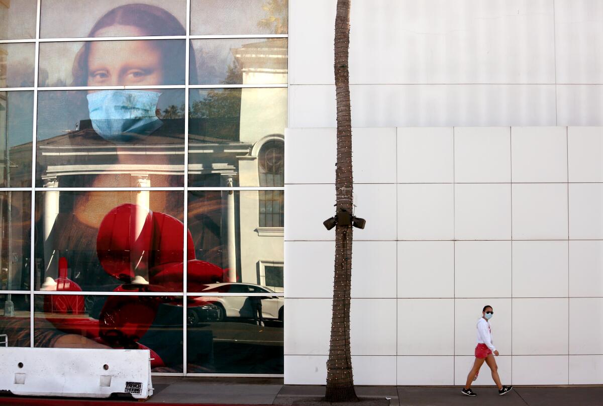 A masked pedestrian walks past a large depiction of Mona Lisa wearing a mask in a building's window