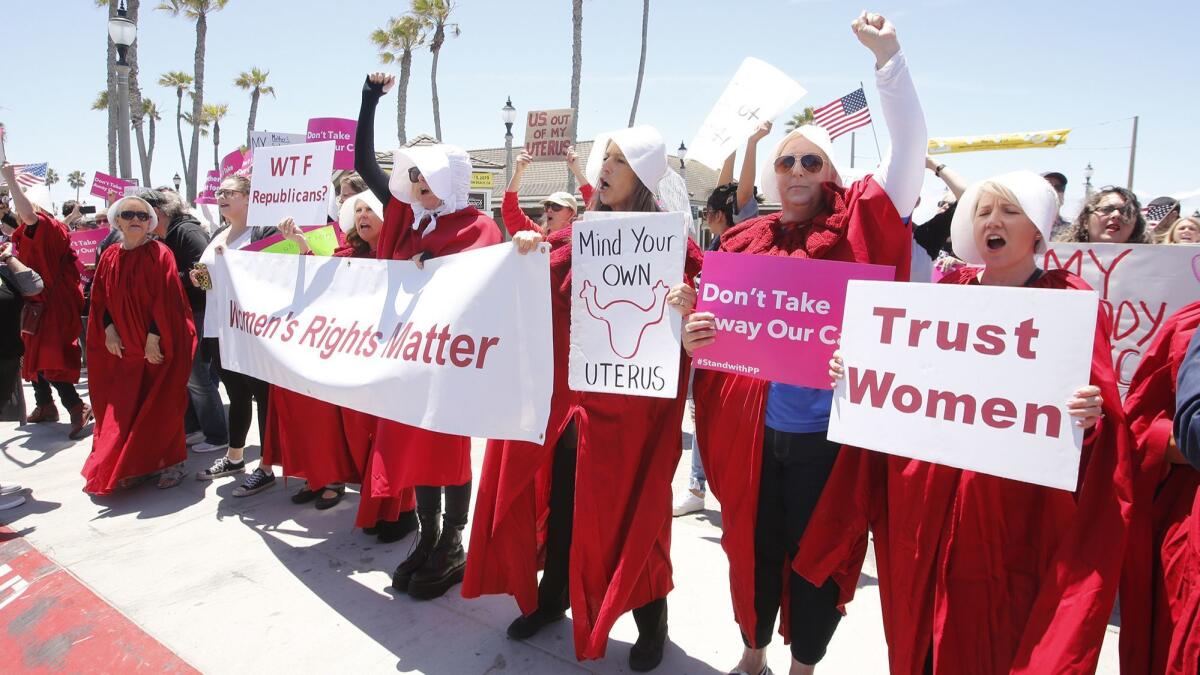 Demonstrators holding signs reading “Women's rights matter,” “Mind your own uterus” and more gather Tuesday at the Huntington Beach Pier for a protest against Alabama’s abortion ban.