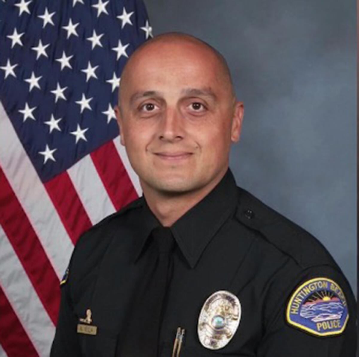 Huntington Beach Police Officer Nicholas Vella in uniform in front of a U.S. flag.