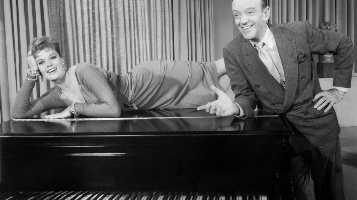 Janis Paige lying on a piano with one hand propping up her head and Fred Astaire leaning on the piano gesturing with one hand
