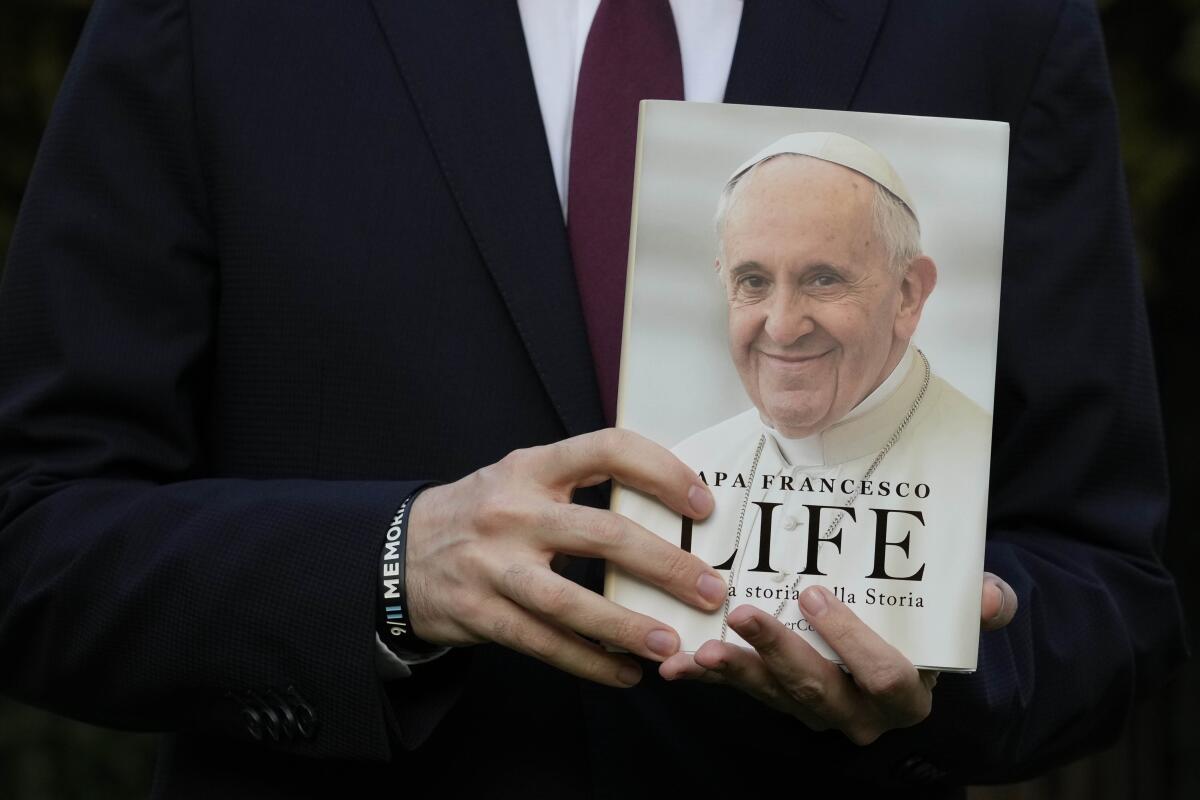 A close-up of hands holding the book 'Life: My Story Through History,' which has a portrait of Pope Francis on the cover