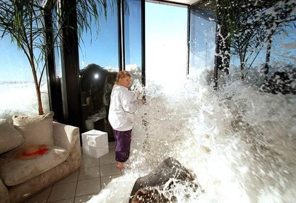 A woman in a white shirt attempts to close the doors to her home as sea water rushes in