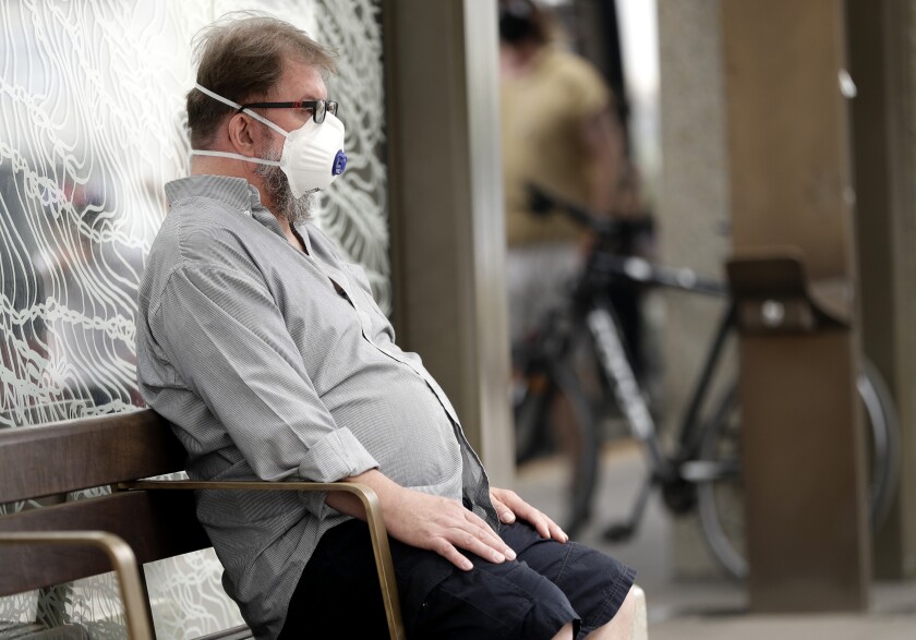 FILE - In this Jan. 2, 2020, file photo, a commuter wears a mask as smoke shrouds the Australian capital of Canberra, Australia. It's an unprecedented dilemma for Australians accustomed to blue skies and sunny days that has raised fears for the long-term health consequences if prolonged exposure to choking smoke becomes the new summer norm. (AP Photo/Mark Baker, File)