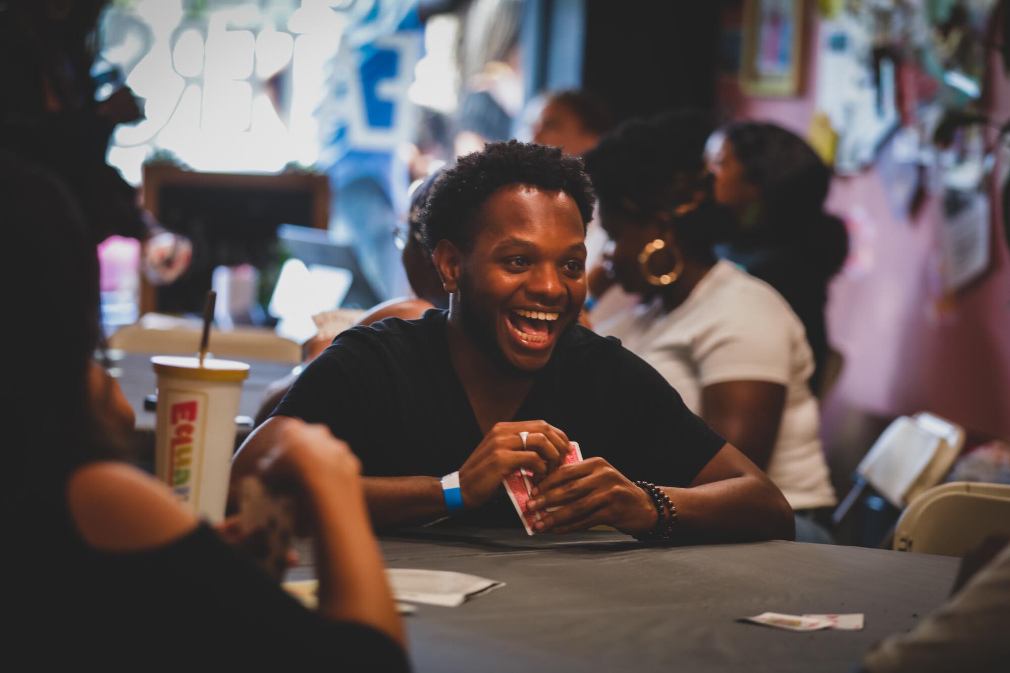 Un homme avec un grand sourire sur son visage tient une main de cartes à une table de jeu