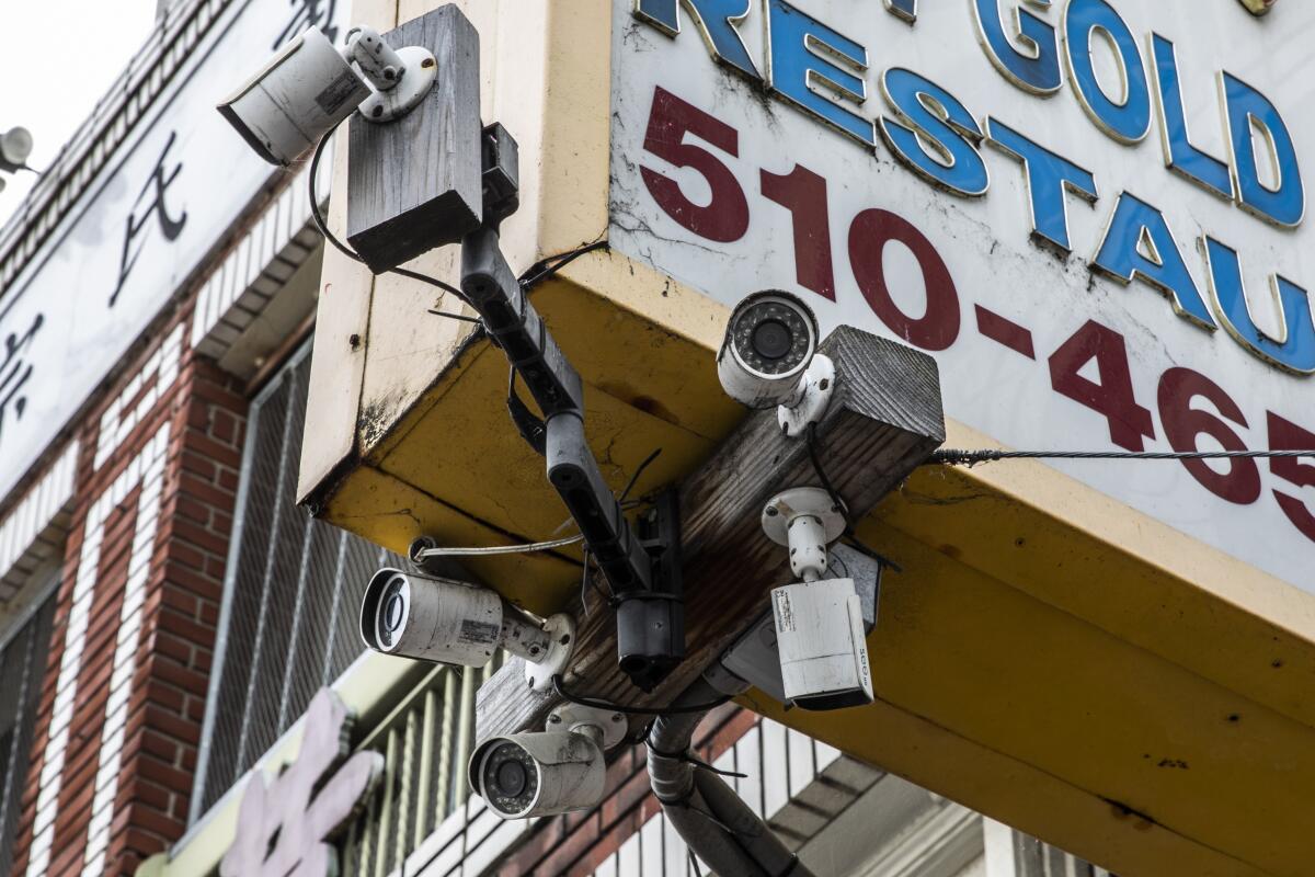 Surveillance cameras are seen mounted on an overhead storefront sign in the Chinatown district of Oakland, California.