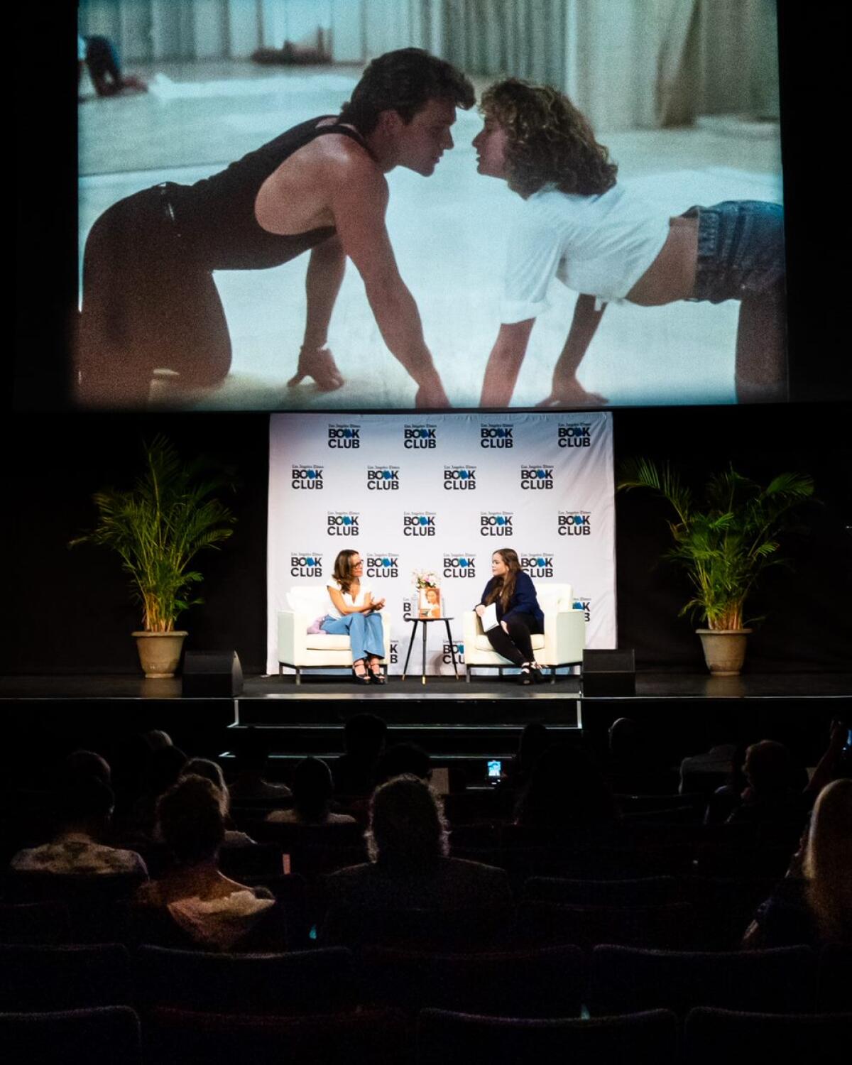 Two women sit onstage as a clip from "Dirty Dancing" plays on a screen above their heads.