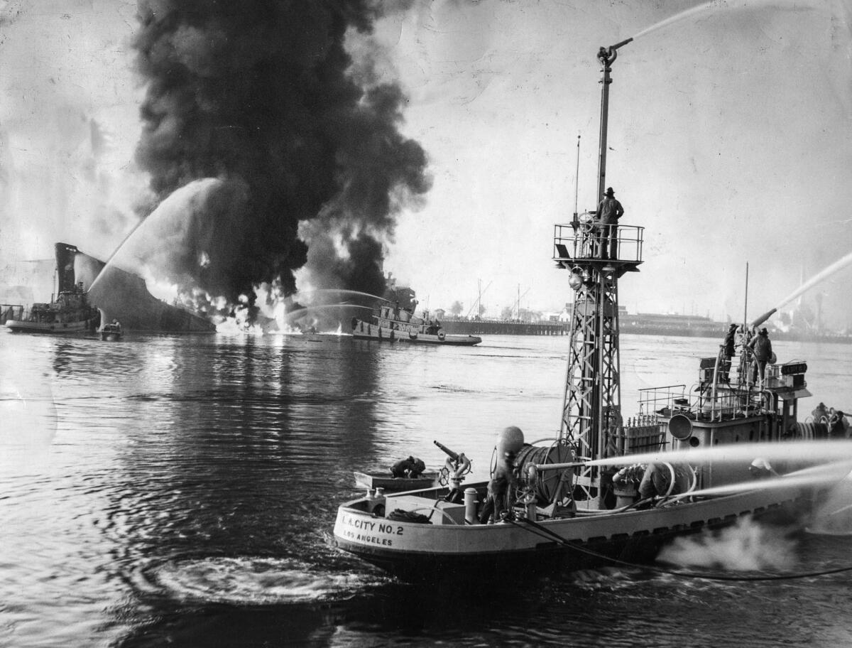 June 22, 1947: Fireboats aim streams of water on the burning tanker Markay, background, after explosion rocked harbor. Fireboat in foreground battles blaze started by burning gasoline on another dock.