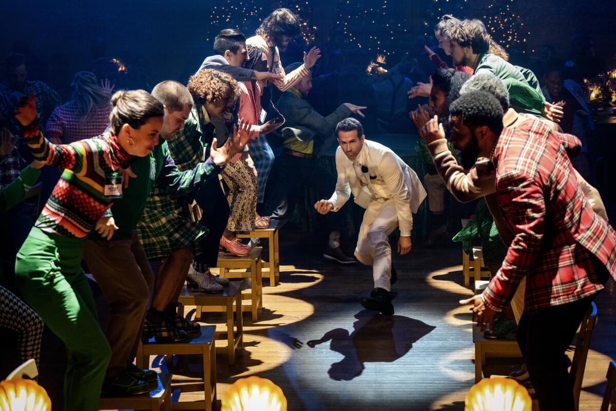 A man in a white suit dances between people standing on chairs