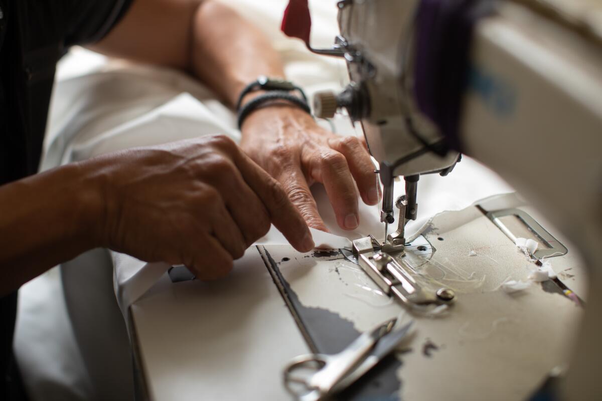A closeup of hands guiding white fabric into the presser foot of a sewing machine