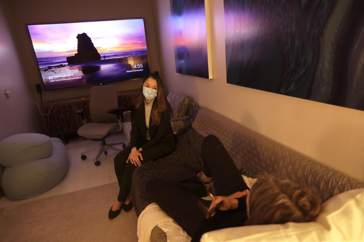 A therapist wearing a mask sits near a client lying on a couch