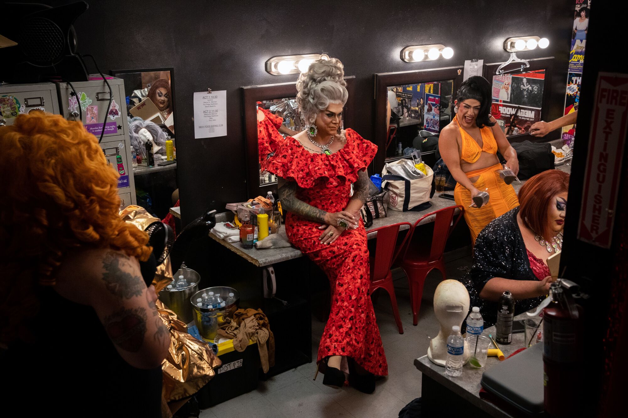 Several drag queens in colorful gowns wait backstage to perform.