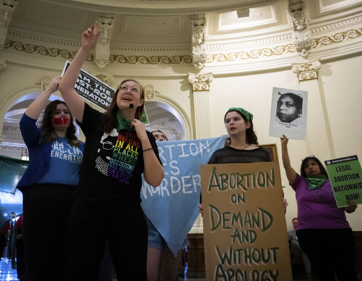 Women hold signs advocating for reproductive rights and one sings into a mic in the rotunda of the Texas State Capitol.