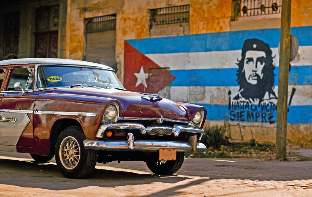 An old Plymouth classic car passes a Cuban flag and Che Guevara mural painted on an eroded wall in Old Havana.
