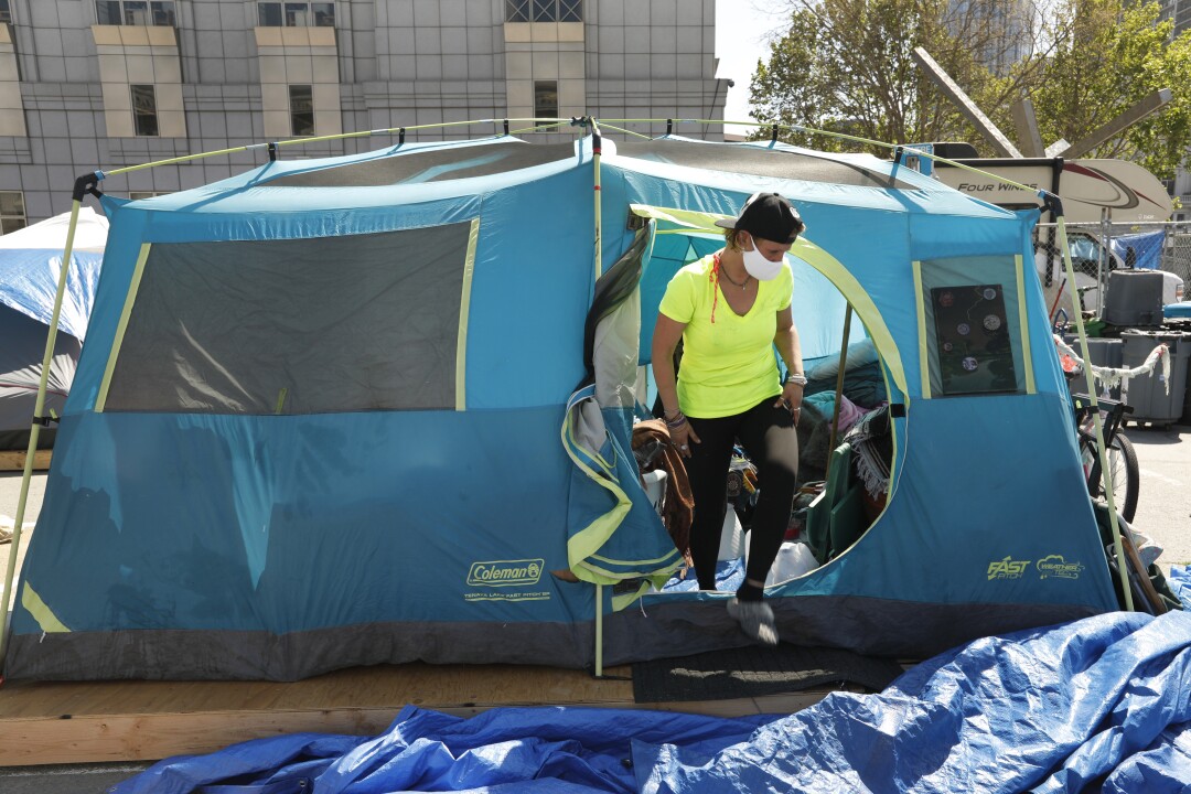 A masked person walks out of a tent