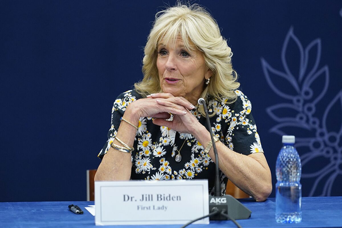 First Lady Jill Biden sits at a table with her fingers laced together beneath her chin