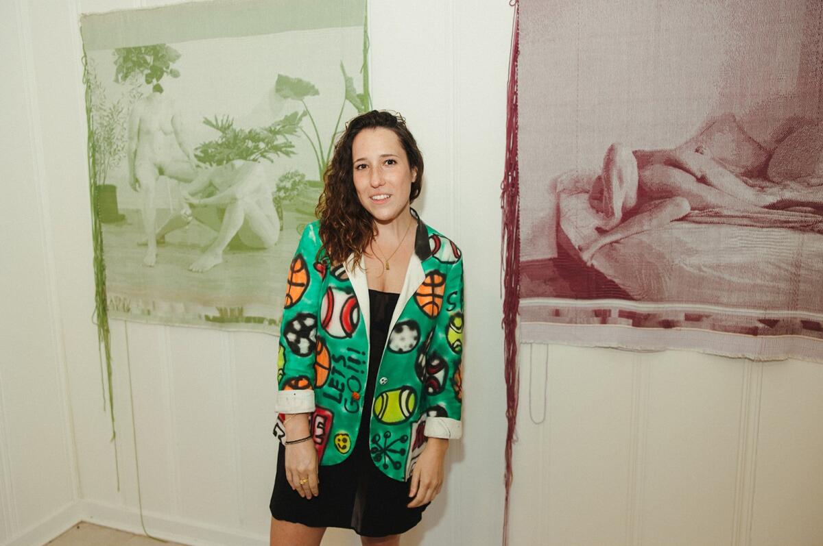 An artist standing in front of her textile artwork of headless figures.
