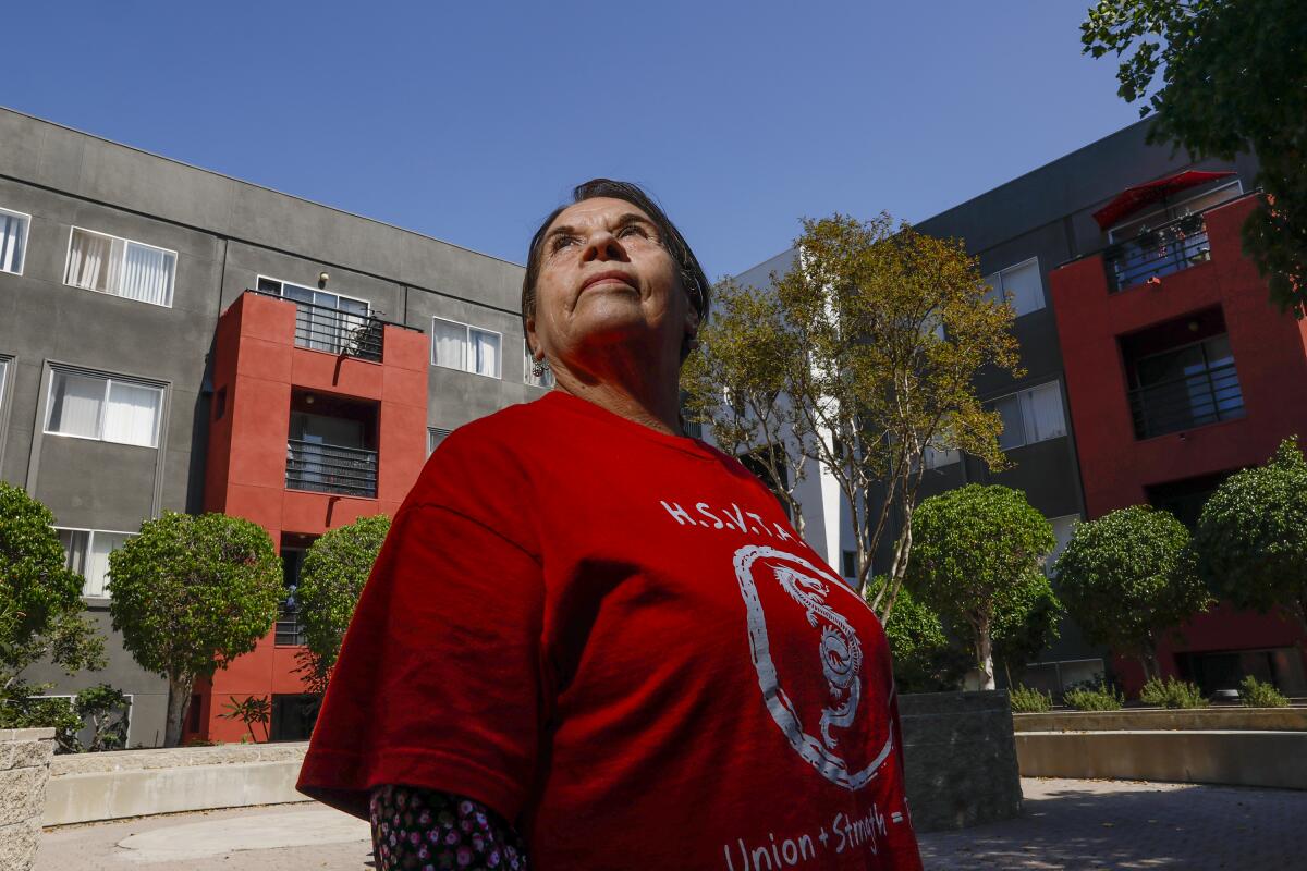 A woman in a red shirt looks up. Behind her is an apartment complex with trees outside