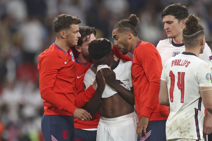 FILE - England players comfort teammate Bukayo Saka after he failed to score a penalty during a penalty shootout after extra time during of the Euro 2020 soccer championship final match between England and Italy at Wembley stadium in London, Sunday, July 11, 2021. Missing penalties in a major international soccer final was bad enough for three Black players, Marcus Rashford, Jadon Sancho and Bukayo Saka, who were on England's national team. Being subjected to a torrent of racial abuse on social media in the aftermath made it even worse. Saka, who has more than 1 million followers on Twitter, remains on social media despite the abuse after England's Euro 2020 loss. (Carl Recine/Pool Photo via AP, File)
