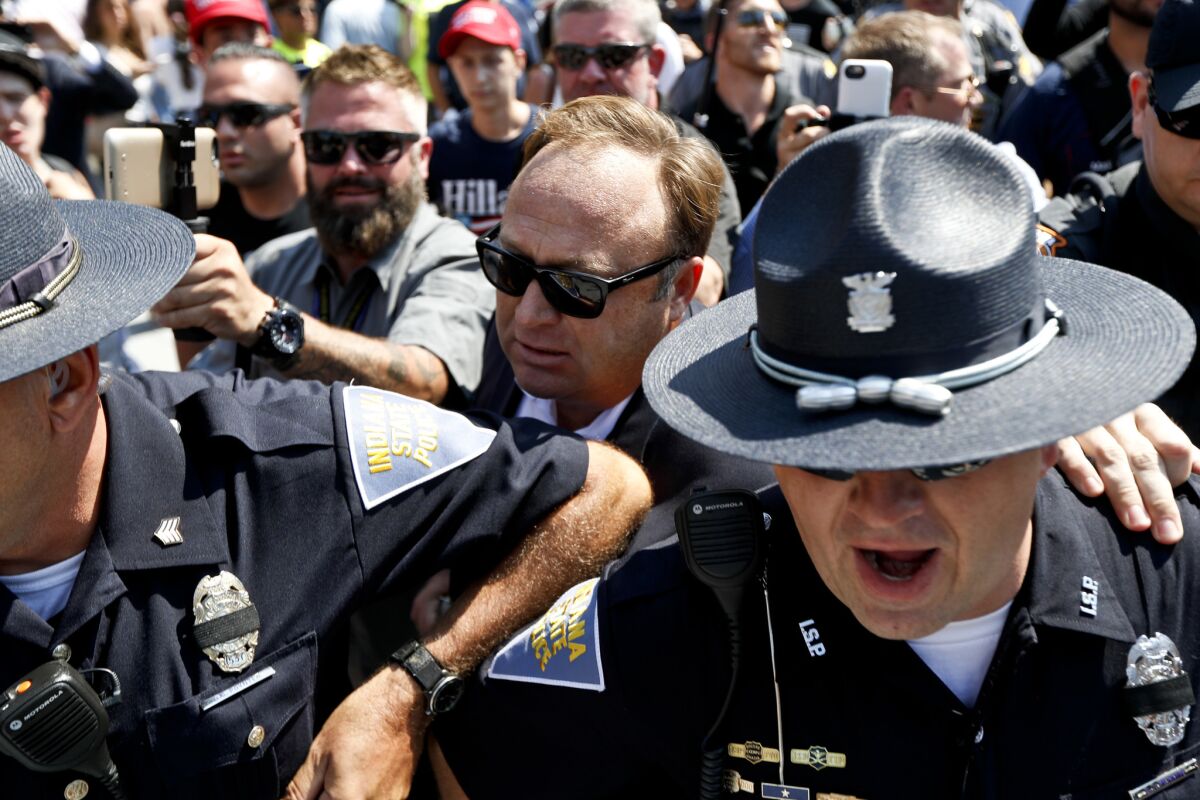 Alex Jones, center, an American conspiracy theorist and radio show host, is escorted out of a crowd of protesters after a scuffle with some of them. (John Minchillo / Associated Press)