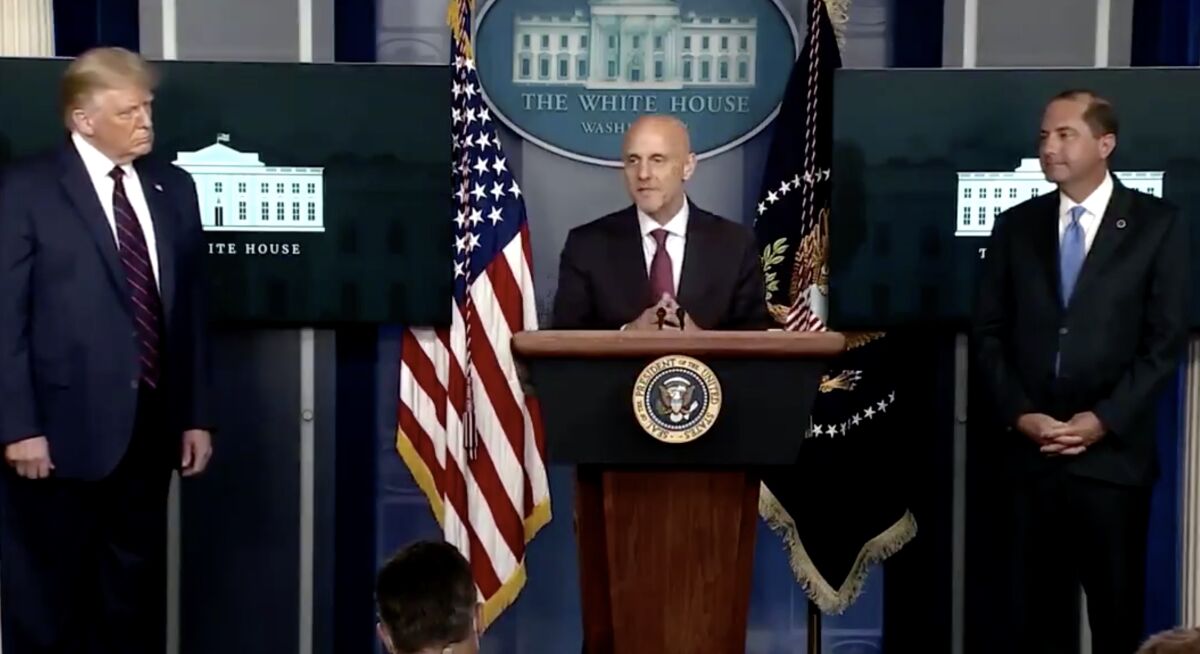 Dr. Stephen Hahn speaks at a White House briefing at a lectern while flanked by two men