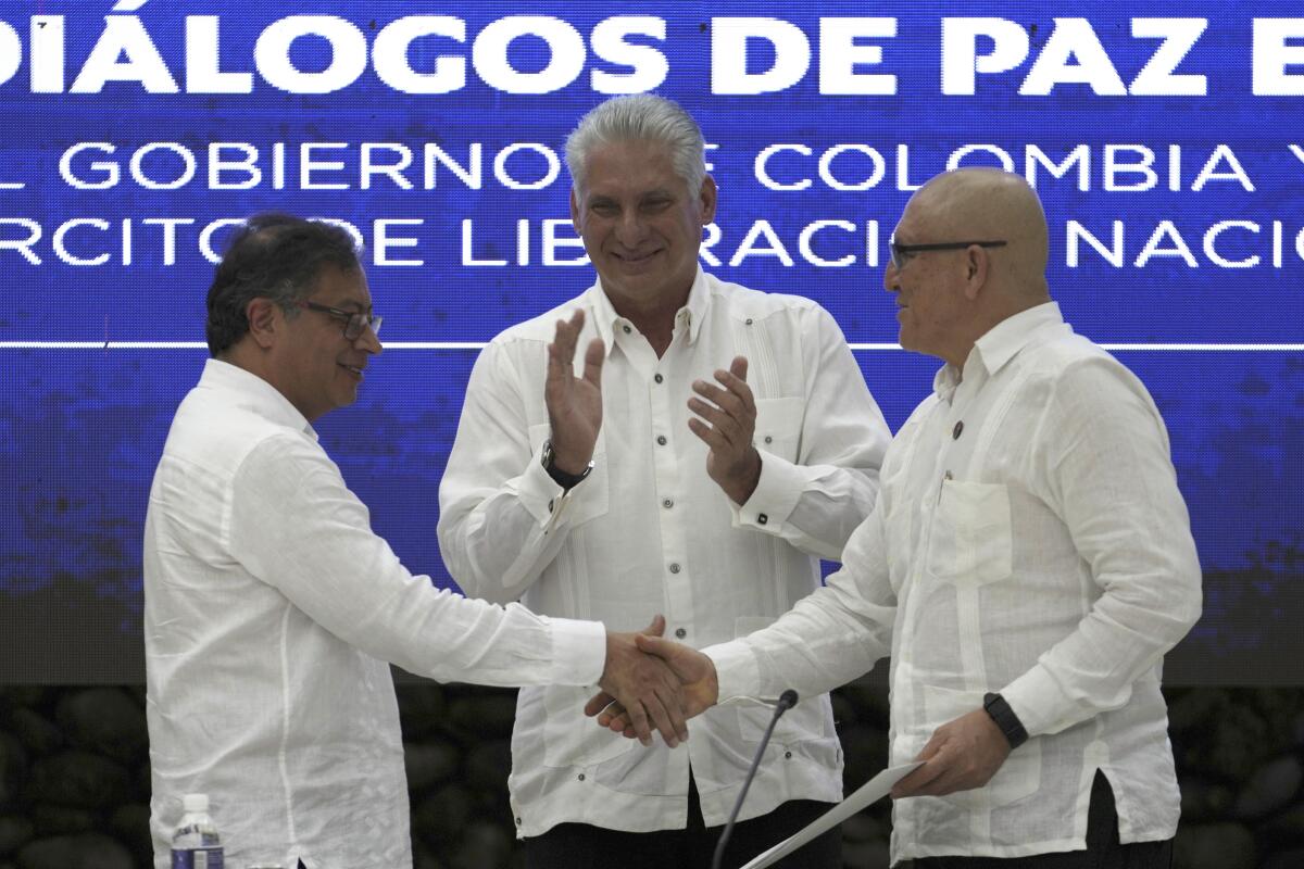 Colombian President Gustavo Petro shaking hands with rebel leader as another man applauds